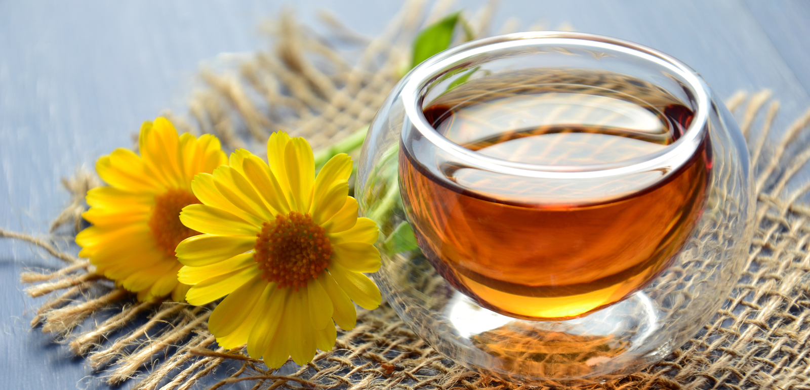 listen to your tea image of tea in a glass cup with two yellow daisies on a hessian mat