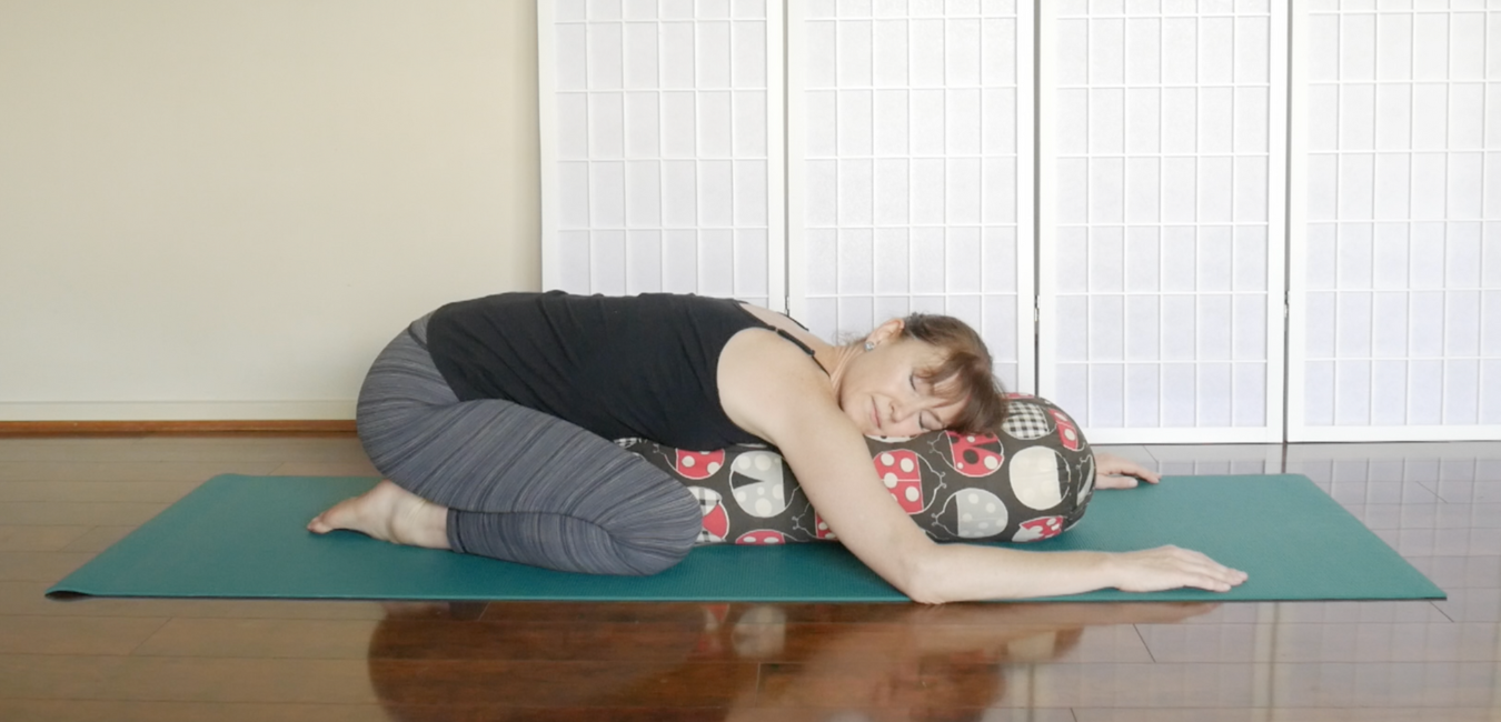 child's pose supported by bolster with arms on floor alongside